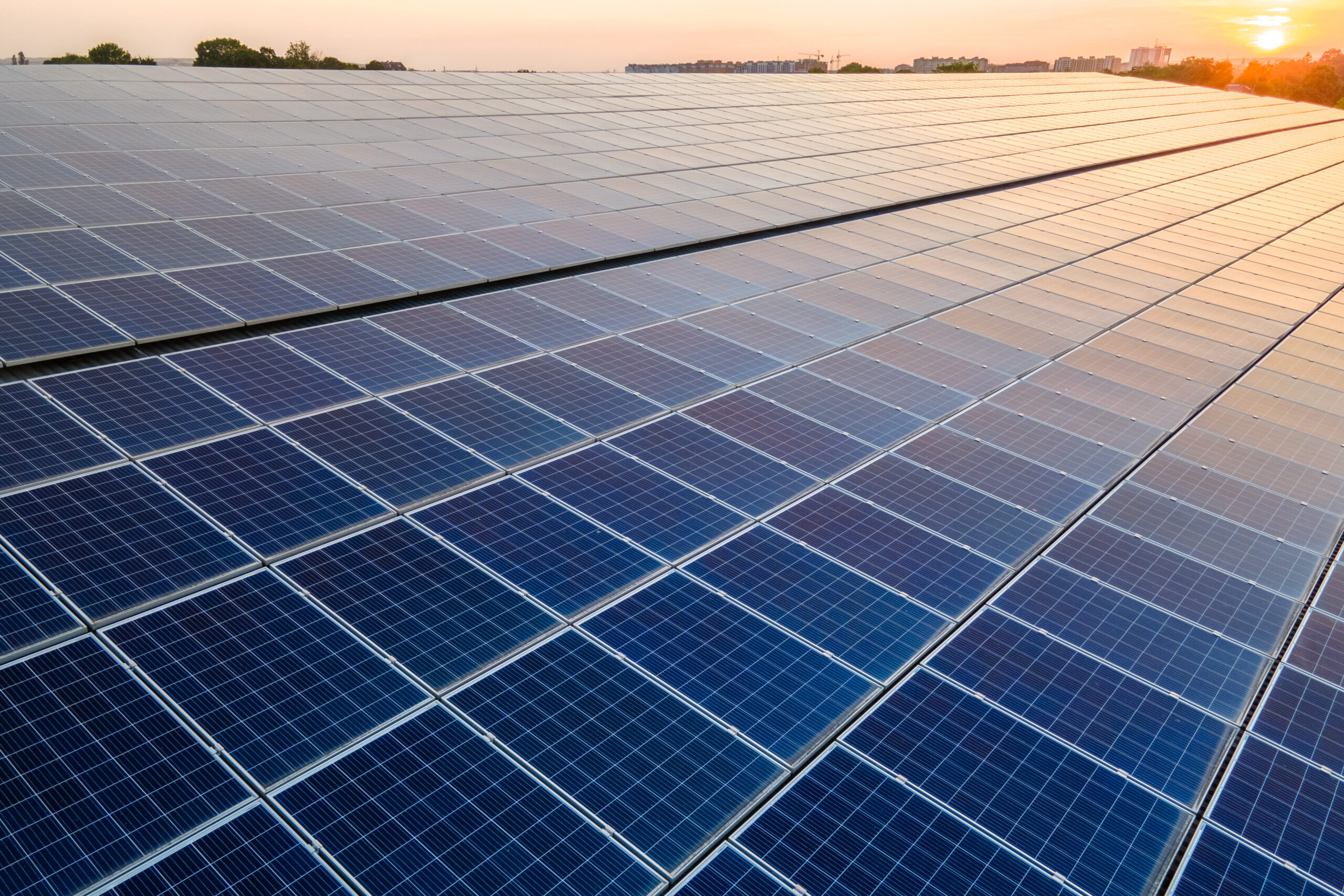 Blue photovoltaic solar panels mounted on building roof for producing clean ecological electricity at sunset. Production of renewable energy concept.